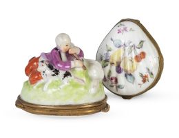 667.  Lote de dos cajitas de porcelana esmaltada: una con pastor tocando la flauta con perro y dos ovejas en la tapa, Francia, S. XIX; y otra en forma de venera con frutos y decoración floral, con marcas de París, S. XIX.